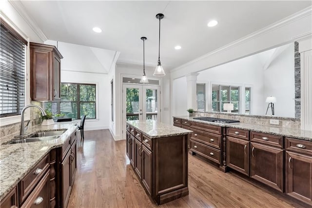 kitchen with sink, hanging light fixtures, light stone counters, light hardwood / wood-style flooring, and stainless steel gas stovetop