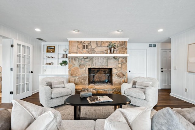 living area with visible vents, built in features, a stone fireplace, and wood finished floors