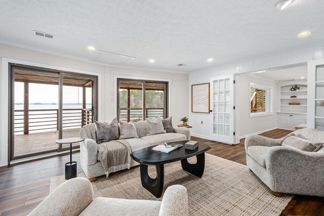 living room with visible vents, built in features, ornamental molding, wood finished floors, and a textured ceiling