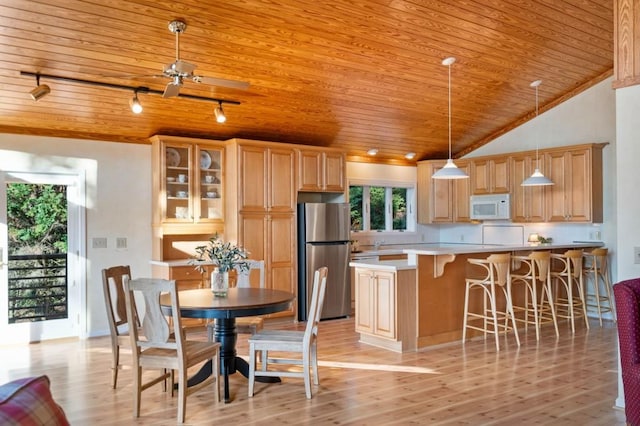 kitchen featuring white microwave, freestanding refrigerator, light wood-style floors, wooden ceiling, and a kitchen breakfast bar