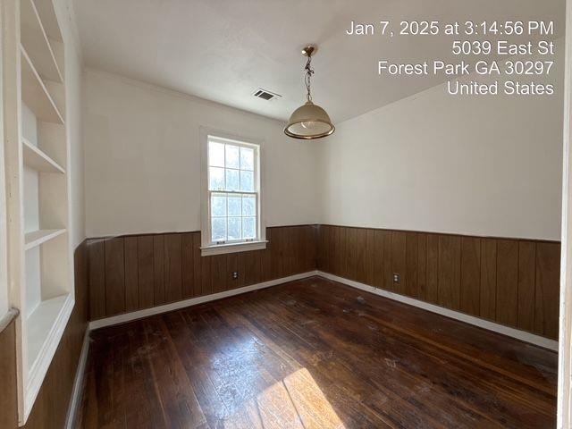 unfurnished room featuring a wainscoted wall, wood walls, wood-type flooring, and visible vents