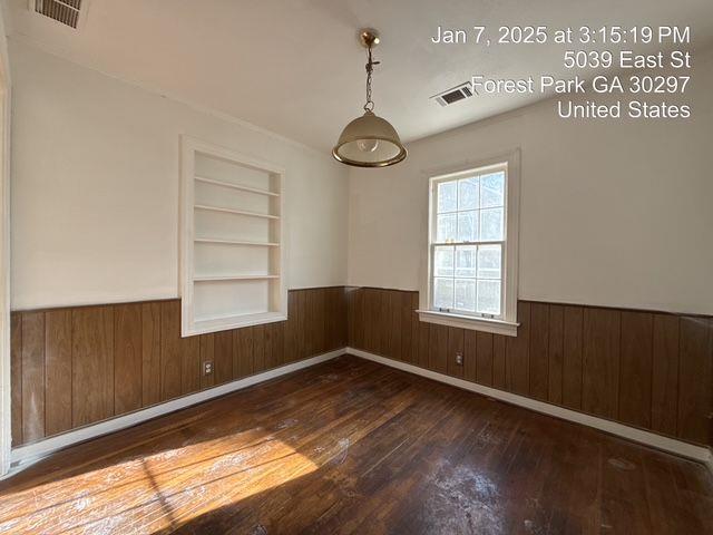 unfurnished room with a wainscoted wall, wood-type flooring, built in shelves, and visible vents
