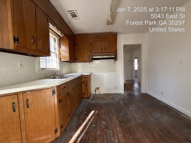 kitchen with dark wood-style flooring, visible vents, brown cabinetry, under cabinet range hood, and baseboards