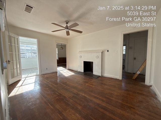 unfurnished living room featuring visible vents, a fireplace with raised hearth, baseboards, and wood finished floors