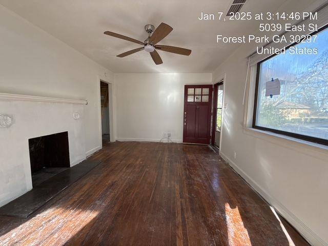 entryway featuring a fireplace with raised hearth, ceiling fan, wood finished floors, and baseboards