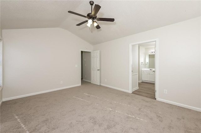 unfurnished bedroom with carpet flooring, ceiling fan, ensuite bath, and vaulted ceiling