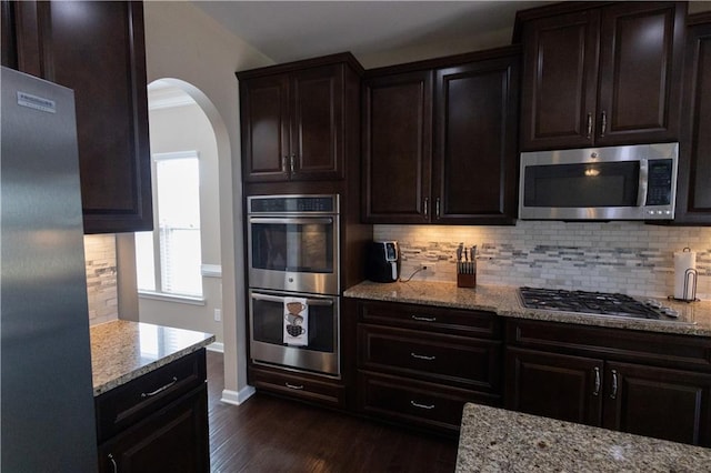 kitchen featuring light stone counters, stainless steel appliances, dark wood-type flooring, and backsplash