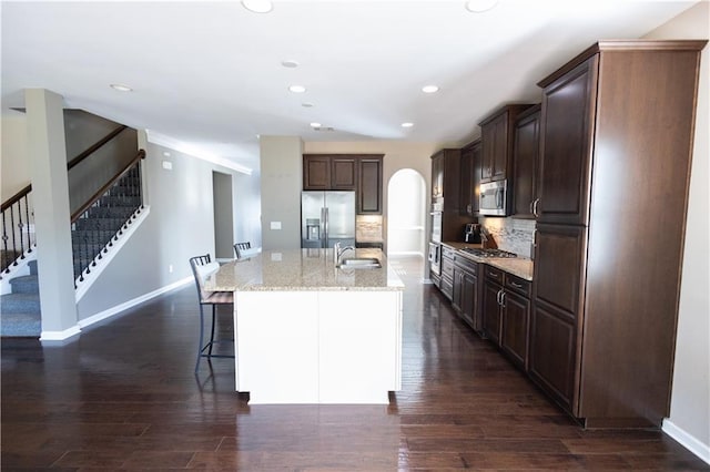 kitchen with a kitchen island with sink, backsplash, dark hardwood / wood-style flooring, a breakfast bar, and appliances with stainless steel finishes