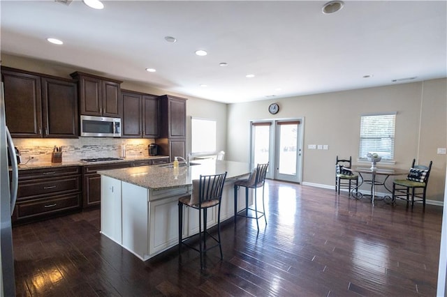 kitchen featuring stainless steel appliances, an island with sink, tasteful backsplash, a kitchen bar, and sink