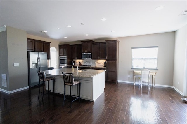 kitchen featuring a center island with sink, decorative backsplash, a kitchen bar, dark hardwood / wood-style flooring, and appliances with stainless steel finishes