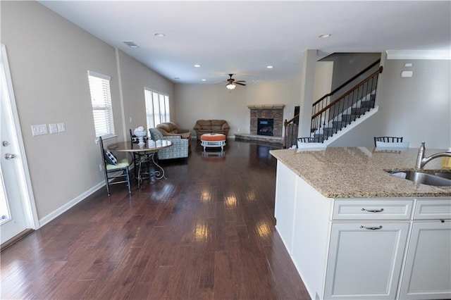 kitchen with sink, white cabinets, light stone countertops, dark hardwood / wood-style floors, and a stone fireplace