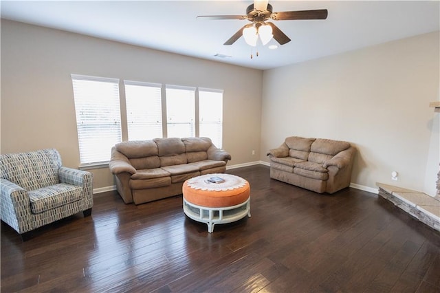 living room featuring ceiling fan, dark hardwood / wood-style flooring, and a stone fireplace