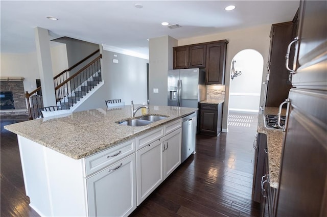 kitchen featuring a stone fireplace, stainless steel appliances, an island with sink, sink, and white cabinetry