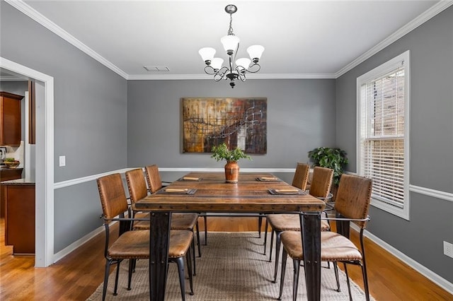 dining space with wood-type flooring, an inviting chandelier, and crown molding