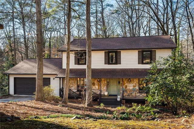 traditional-style home with roof with shingles, a porch, concrete driveway, an attached garage, and stone siding