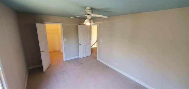 unfurnished bedroom with a walk in closet, a closet, light carpet, ceiling fan, and baseboards