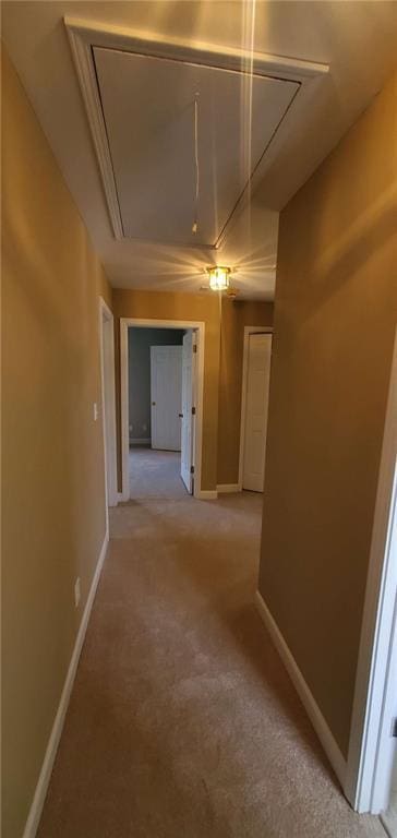 hallway with attic access, light colored carpet, and baseboards