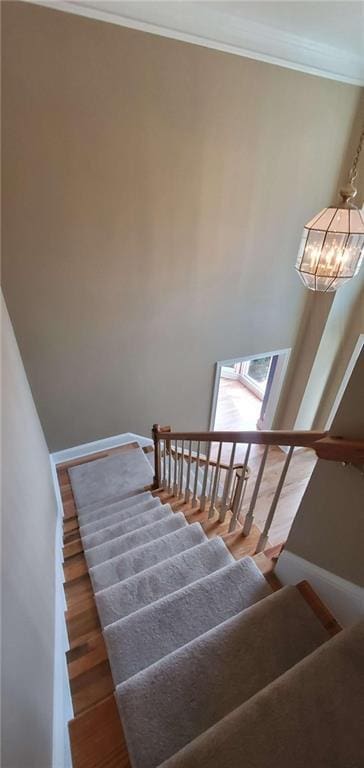 stairs featuring ornamental molding, an inviting chandelier, baseboards, and wood finished floors