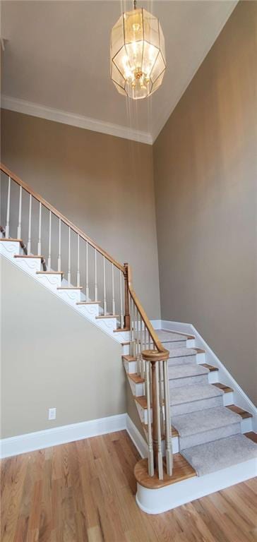 staircase featuring a notable chandelier, baseboards, ornamental molding, and wood finished floors