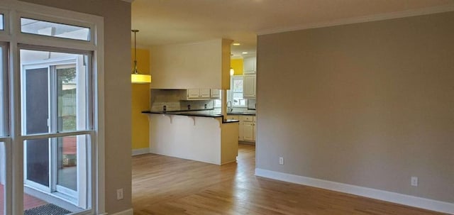 kitchen featuring light wood finished floors, a kitchen bar, dark countertops, a peninsula, and baseboards