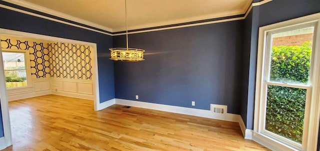 spare room featuring visible vents, wainscoting, wood finished floors, an inviting chandelier, and crown molding