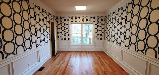 spare room featuring a wainscoted wall, crown molding, light wood finished floors, visible vents, and a decorative wall