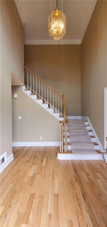 staircase featuring a chandelier, crown molding, baseboards, and wood finished floors