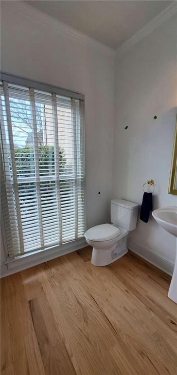 half bathroom with toilet, baseboards, ornamental molding, and wood finished floors