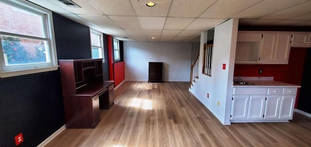 interior space with light wood-type flooring, visible vents, a drop ceiling, and stairs