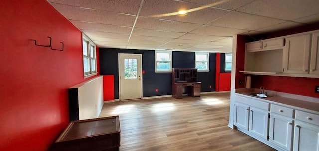 interior space with light wood-type flooring, a sink, baseboards, and a paneled ceiling