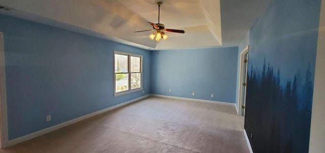 empty room with carpet floors, a tray ceiling, ceiling fan, and baseboards