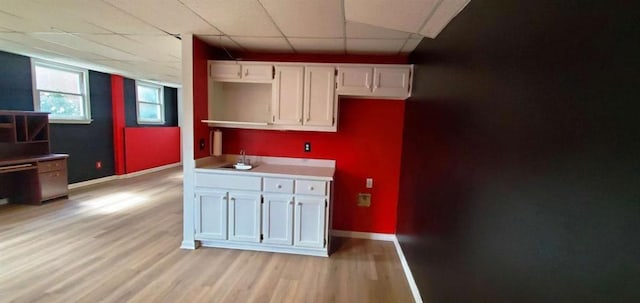 kitchen featuring baseboards, a drop ceiling, light wood-style flooring, and white cabinets