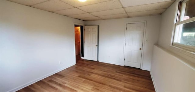 unfurnished bedroom featuring a drop ceiling, baseboards, and wood finished floors