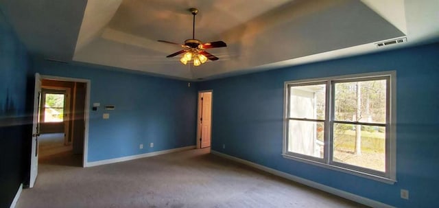 carpeted empty room with a raised ceiling, visible vents, ceiling fan, and baseboards