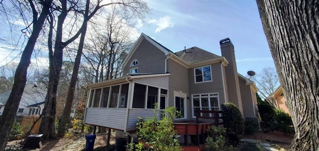 rear view of property with a sunroom, a chimney, and stucco siding