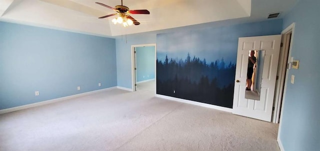 carpeted spare room with a ceiling fan, a tray ceiling, visible vents, and baseboards