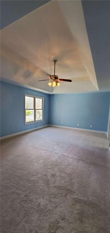 carpeted spare room with ceiling fan, a tray ceiling, and baseboards