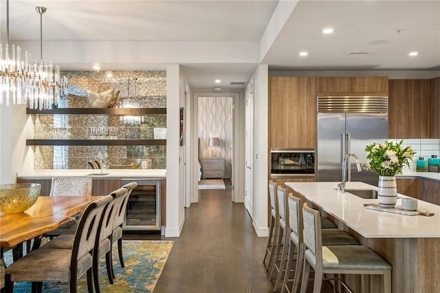 kitchen with sink, hanging light fixtures, wine cooler, built in appliances, and dark hardwood / wood-style floors