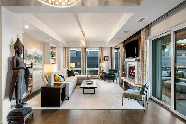 living room with hardwood / wood-style floors, a large fireplace, a raised ceiling, and a chandelier