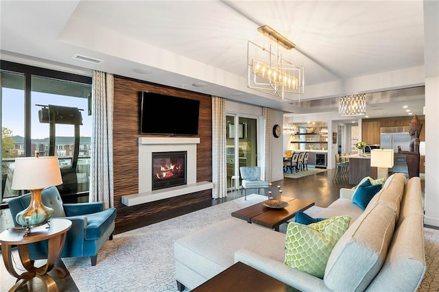 living room featuring a tray ceiling, wood-type flooring, and an inviting chandelier