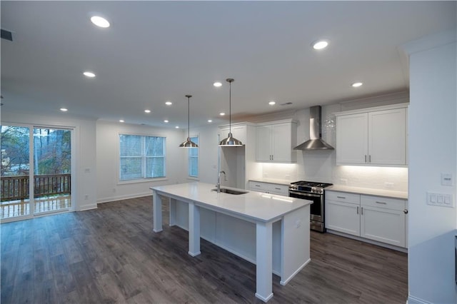 kitchen featuring a center island with sink, hanging light fixtures, stainless steel range with gas cooktop, wall chimney exhaust hood, and sink