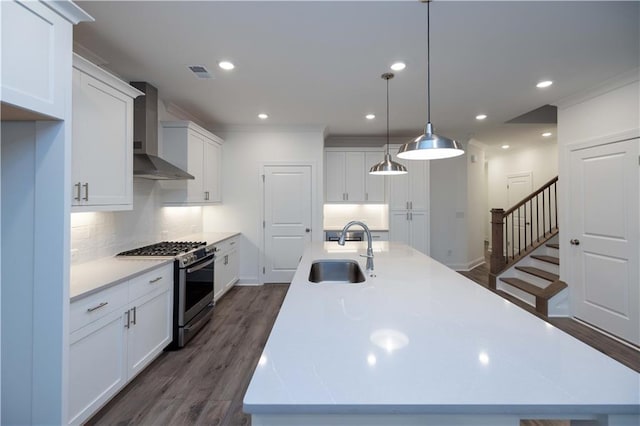 kitchen with white cabinets, gas stove, sink, wall chimney range hood, and decorative light fixtures