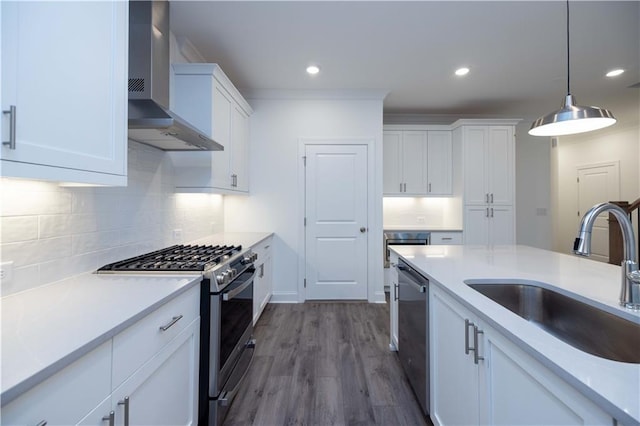 kitchen featuring appliances with stainless steel finishes, pendant lighting, wall chimney exhaust hood, white cabinets, and sink