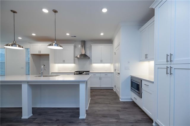 kitchen with sink, white cabinets, wall chimney range hood, and stainless steel microwave