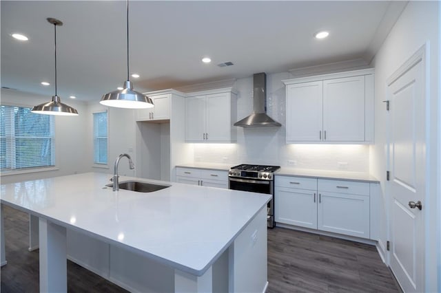 kitchen featuring stainless steel range with gas cooktop, wall chimney exhaust hood, sink, white cabinetry, and decorative light fixtures