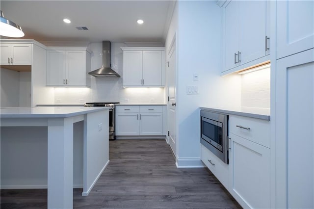 kitchen with wall chimney range hood, dark wood-type flooring, white cabinetry, and appliances with stainless steel finishes