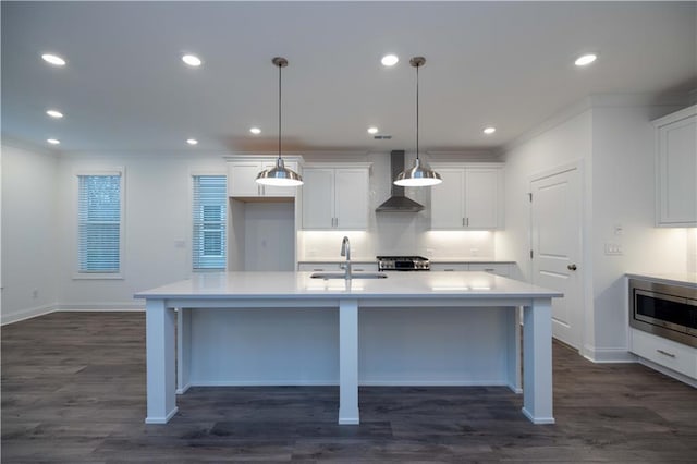 kitchen with wall chimney exhaust hood, hanging light fixtures, a center island with sink, white cabinets, and sink