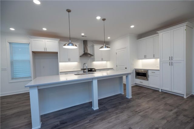 kitchen featuring a kitchen island with sink, pendant lighting, wall chimney exhaust hood, stainless steel microwave, and white cabinetry