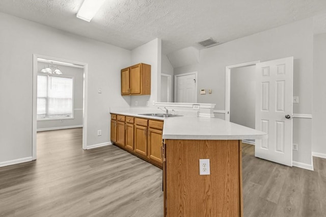 kitchen with sink, an inviting chandelier, a textured ceiling, kitchen peninsula, and light hardwood / wood-style floors