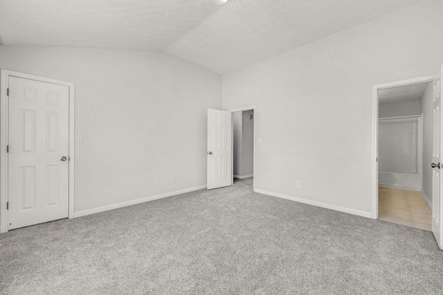 unfurnished bedroom featuring ensuite bath, lofted ceiling, and carpet